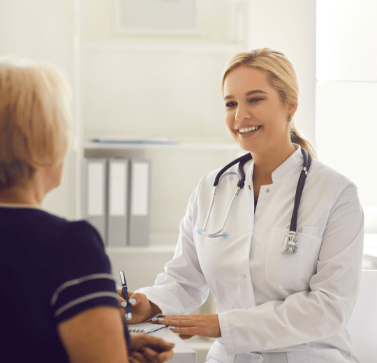 A caucasian woman , 30 years old, blonde hair, wearing a white coat and a stethoscope, talking to a patient in a doctor’s office (2) Comprehensive Primary Care Billing Services