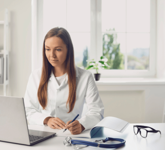 A caucasian woman , 30 years old with white hair, wearing a white coat , writing on a notebook with a laptop , in a doctor’s office Comprehensive Pharmacy Billing Services
