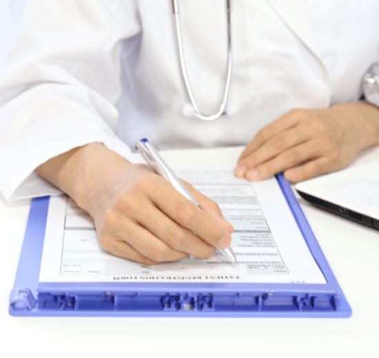 A doctor with dark skin wearing a white coat and stethoscope filling out a patient registration form on a white table How Pharmacy Billing Process Works