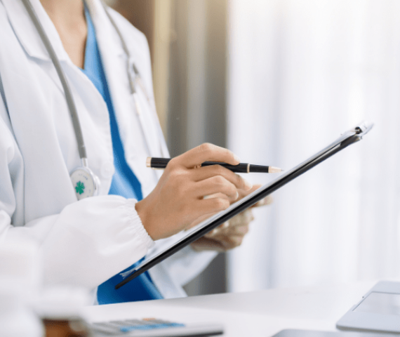 A fair-skinned woman with a white coat and stethoscope writing on a clipboard, in a bright medical office Why Choose HealthbridgeMD for Healthcare Digital Marketing