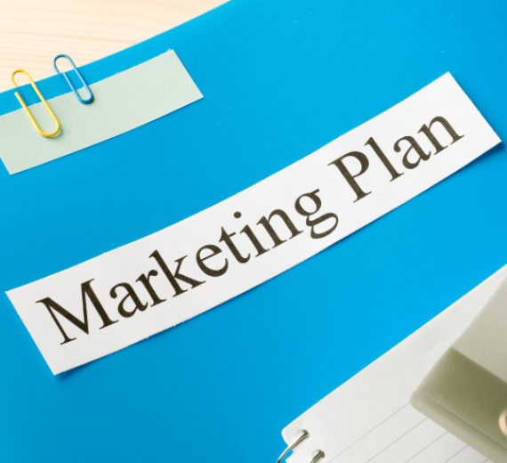 A piece of paper with the words Marketing Plan written on it, a notebook and paper clips on a blue surface How Our Healthcare Digital Marketing Process Works