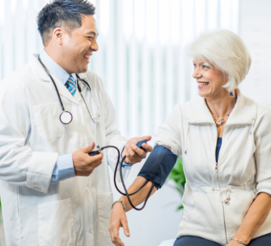An asian man , 35 years old, with a stethoscope, measuring the blood pressure of a caucasian woman , 70 years old, in a doctor’s office pharmacy medical billing services
