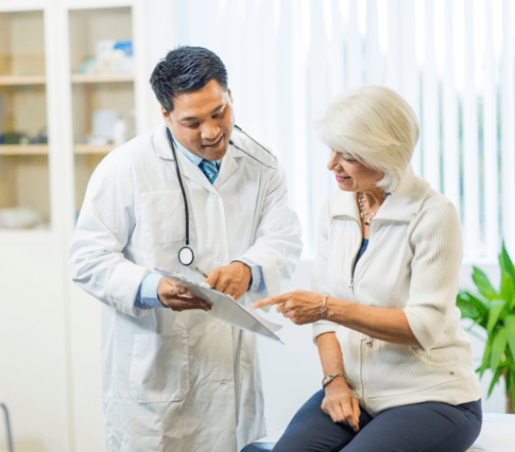 An asian man doctor, 30 years old, with a stethoscope , explaining a document to a caucasian woman , 65 years old, in a doctor’s office Revenue Cycle Management Services - HealthBridgeMD